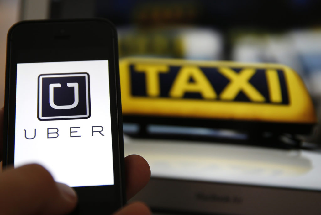 File illustration picture showing the logo of car-sharing service app Uber on a smartphone next to the picture of an official German taxi sign in Frankfurt, September 15, 2014. A Frankfurt court earlier this month instituted a temporary injunction against Uber from offering car-sharing services across Germany. San Francisco-based Uber, which allows users to summon taxi-like services on their smartphones, offers two main services, Uber, its classic low-cost, limousine pick-up service, and Uberpop, a newer ride-sharing service, which connects private drivers to passengers - an established practice in Germany that nonetheless operates in a legal grey area of rules governing commercial transportation.    REUTERS/Kai Pfaffenbach/Files  (GERMANY - Tags: BUSINESS EMPLOYMENT CRIME LAW TRANSPORT)